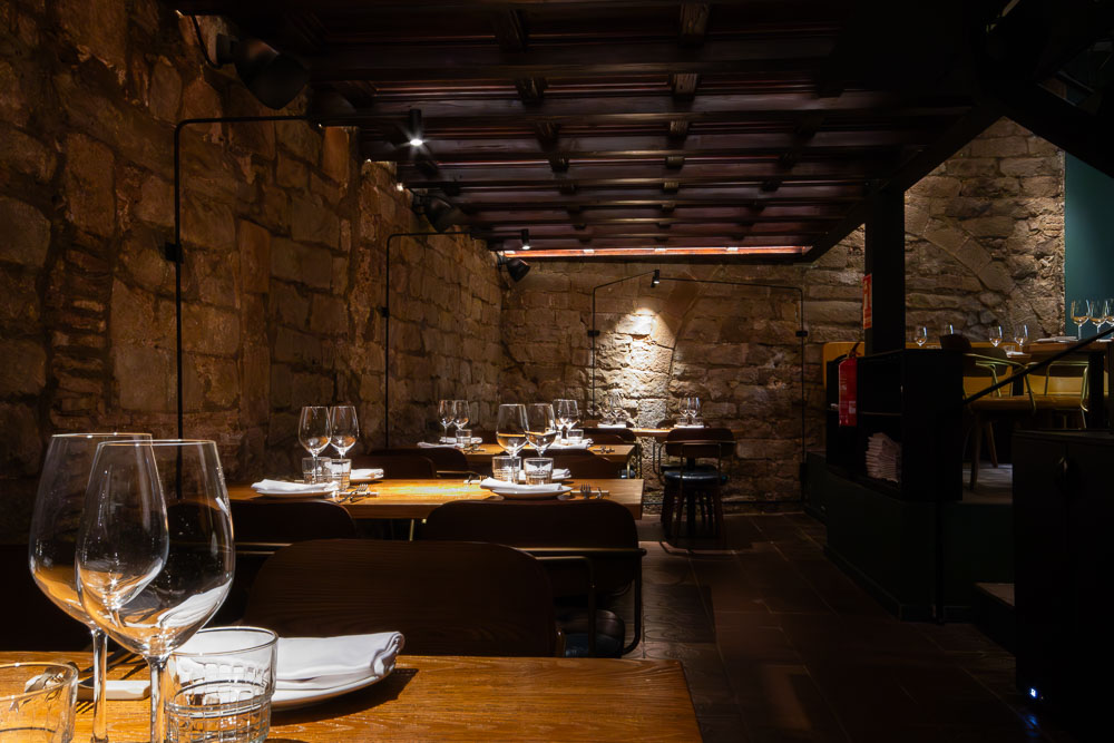 Salón de restaurante en el Born de Barcelona con muros de piedra recuperados e iluminación puntual sobre las mesas.